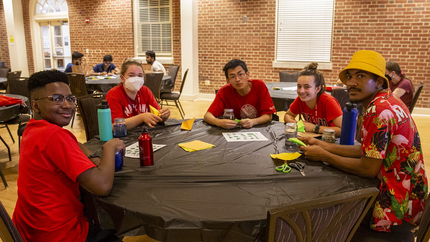 five students sitting at round table doing arts and crafts