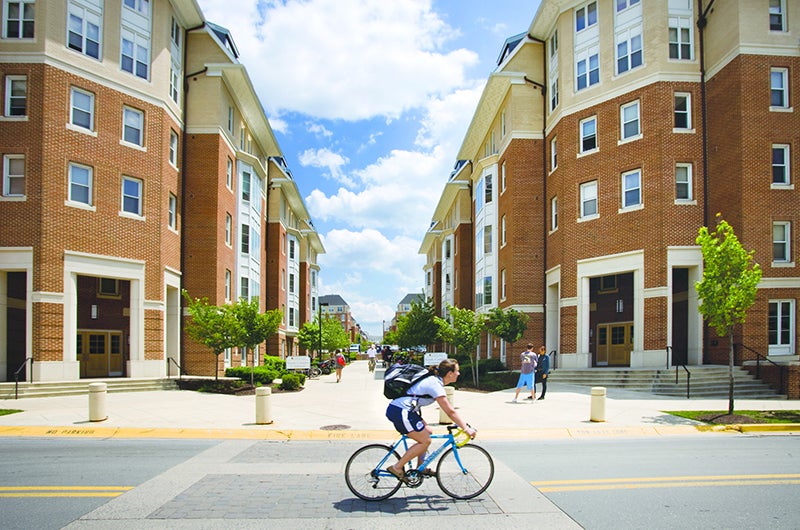 A student rides a blue bicycle past the brick apartment buildings of South Campus Commons.