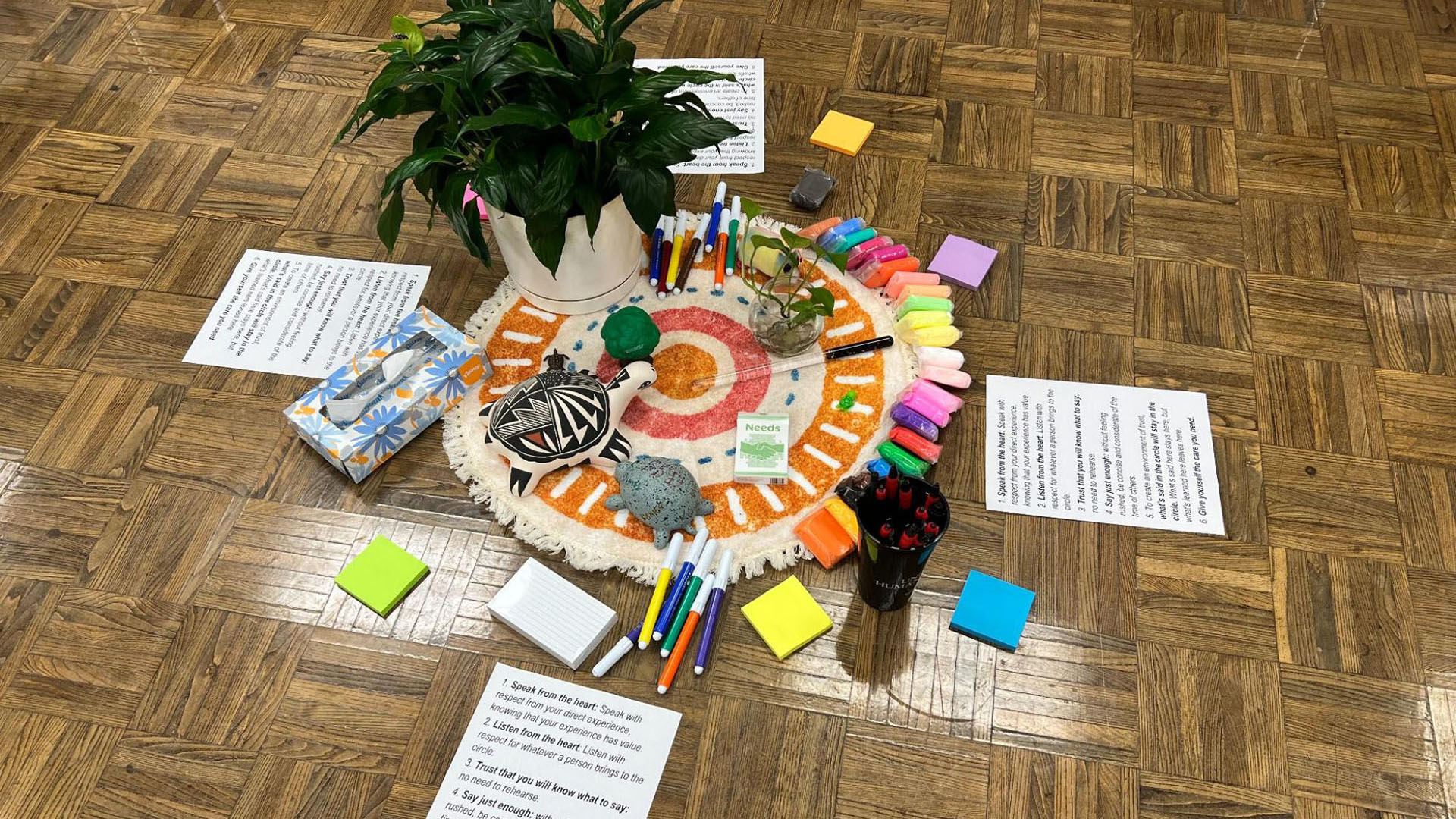 colorful mat with markers, plants, sticky notes, and paper with restorative guidelines surrounding it on the floor.