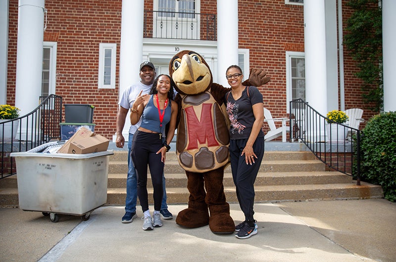 A student and parents pose with Testudo mascot in front of a brick building during move-in.