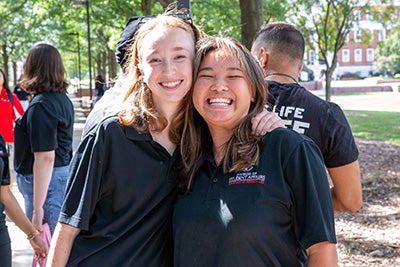 Two smiling Resident Assistants in black polo shirts posing together outdoors during training.