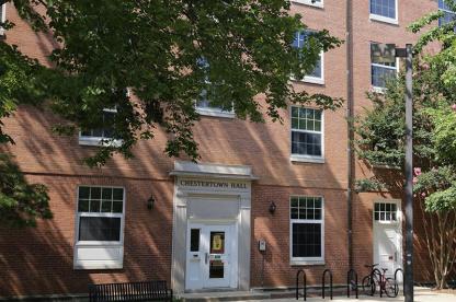 Exterior of brick Chestertown Hall with a white door frame and black bike racks in front.