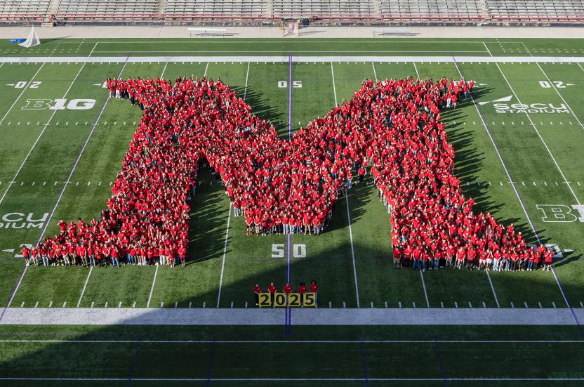 students wearing red shirts in an M formation on the football field for a class photo