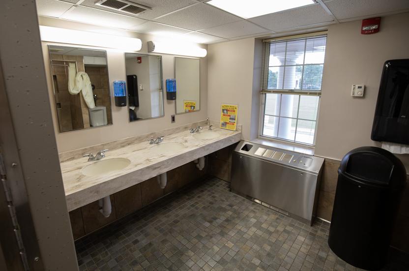 Shared bathroom in a house on the row with a vanity with three sinks, mirrors, and a window.