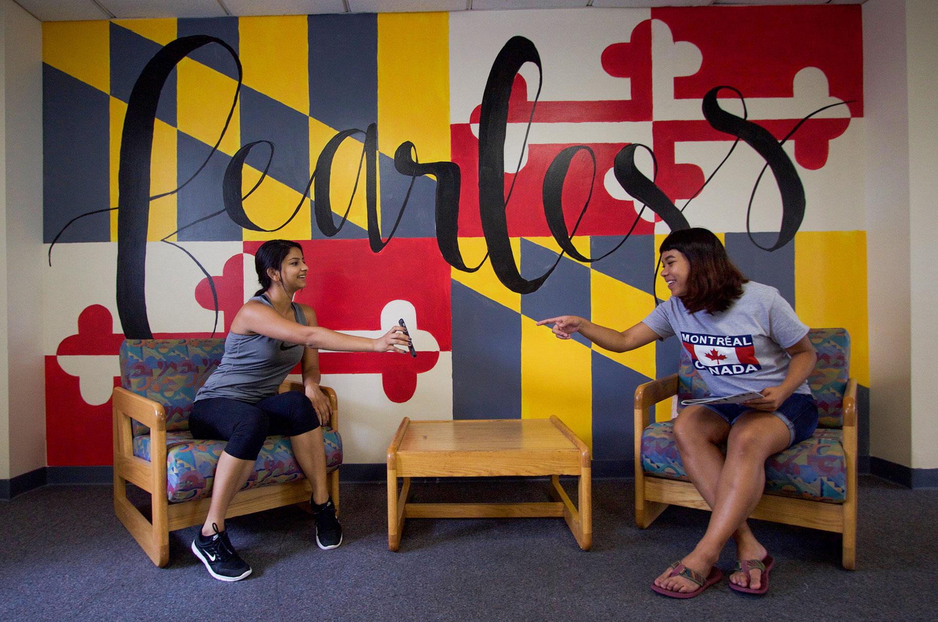 two students in a lounge with a decorative mural in the background