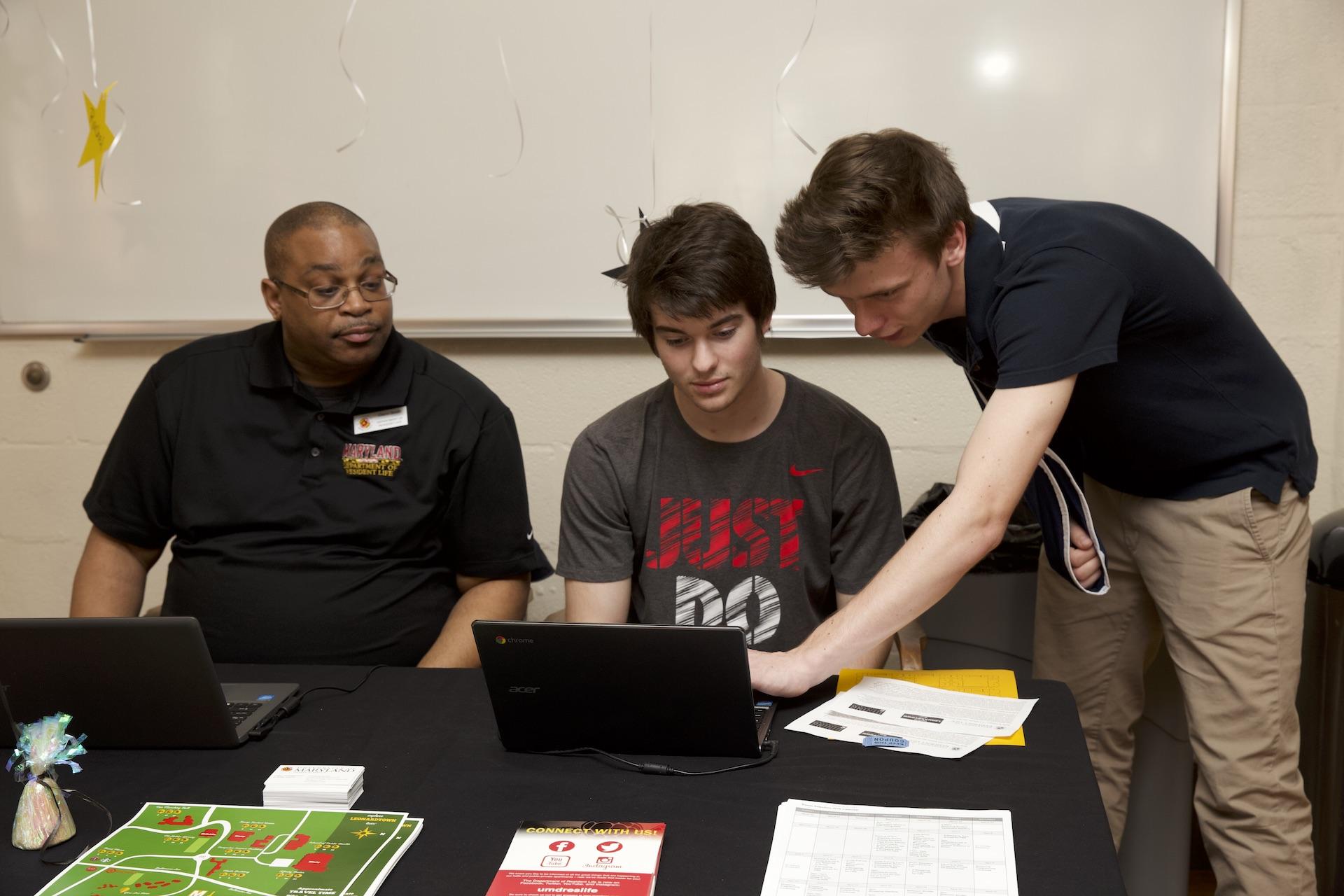 two staff members helping a student on a laptop at an information booth