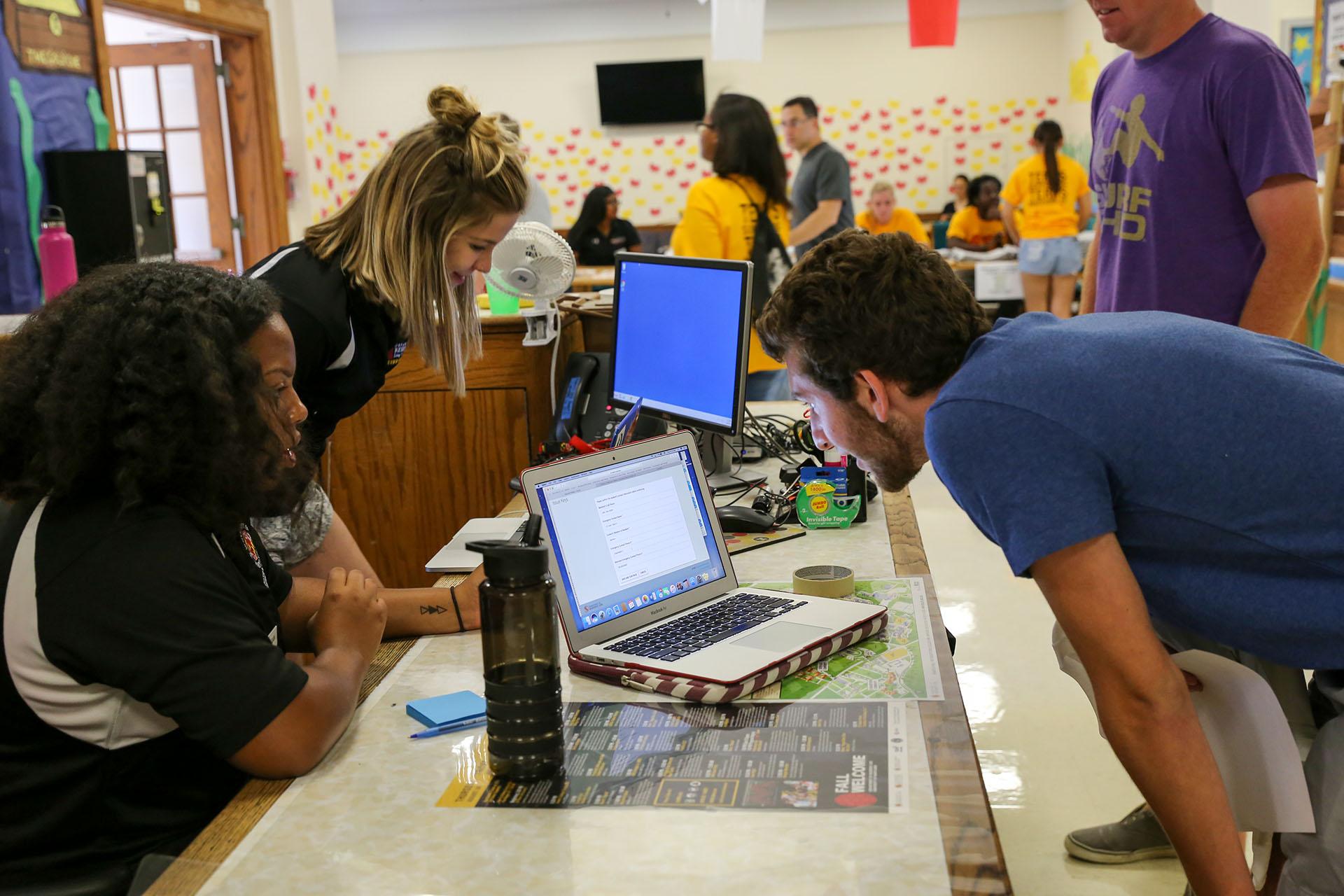 student staff at service desk helping another student who is looking at a laptop screen on the counter