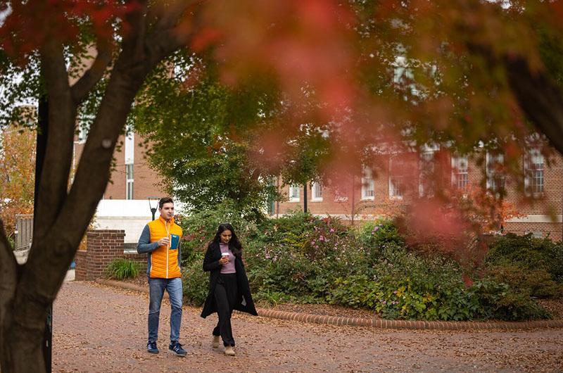 two students walking on campus on a fall day holding to-go coffee cups