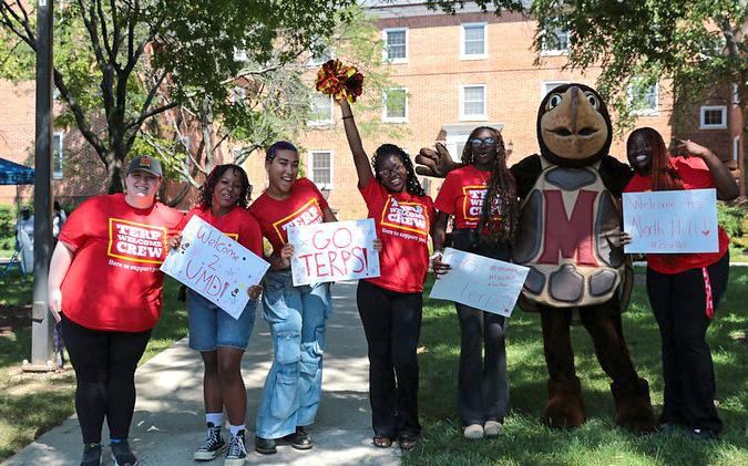 group of terp welcome crew volunteers with signs and pom poms in front of a residence hall with Testudo