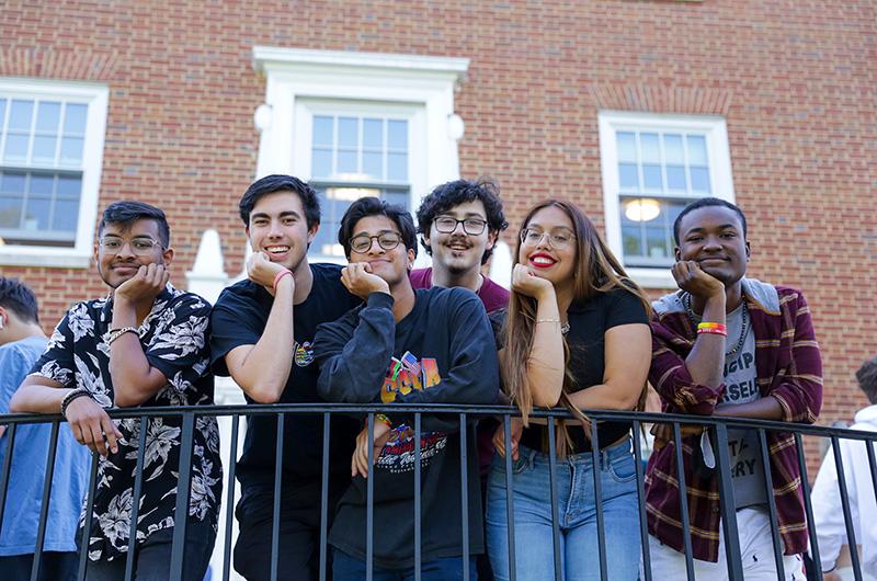group of 6 residential students leaning on a metal fence in front of a residence hall