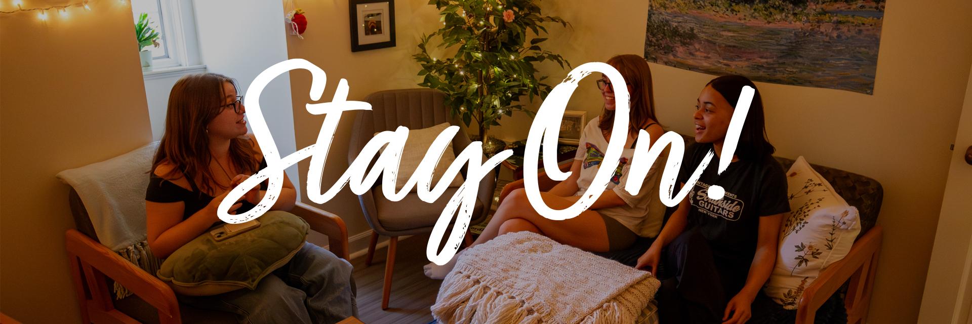 Three college students relax and talk in a cozy, decorated living room, with the large text "Stay On!" overlay.