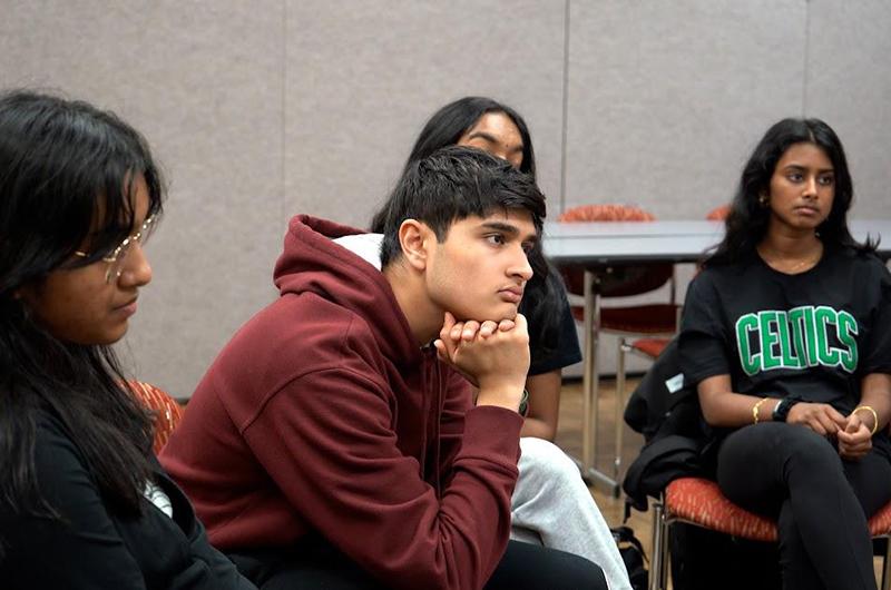 Four students seated indoors, listening attentively during a group discussion.
