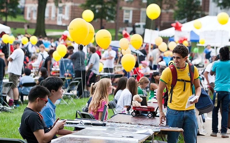student wearing Brazil national soccer jersey checking out a booth during the first look fair, balloons and tents blurred in the background