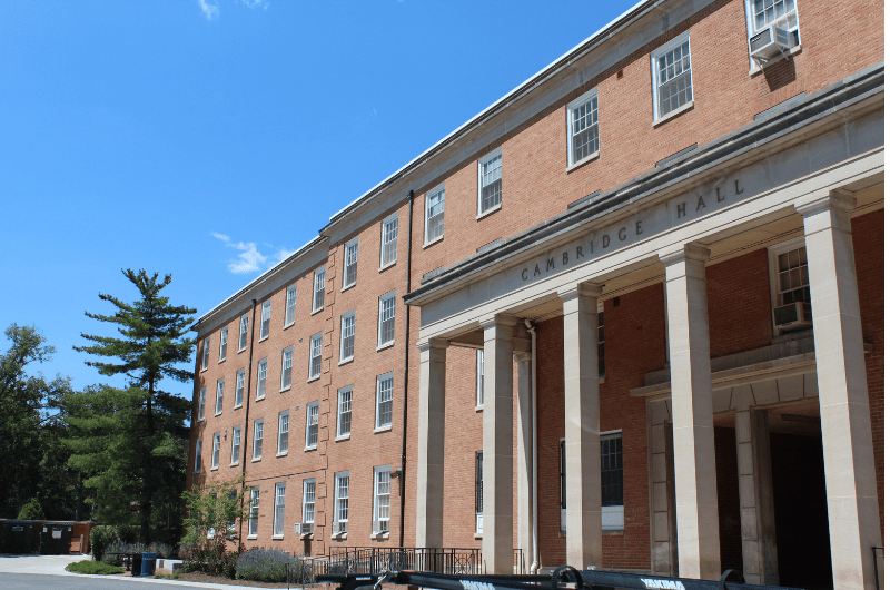 Exterior of brick Cambridge Hall with white pillars under a clear blue sky.