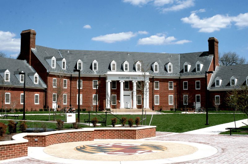 Exterior of Harford Hall, a brick building with white pillars and dormers behind a brick courtyard.