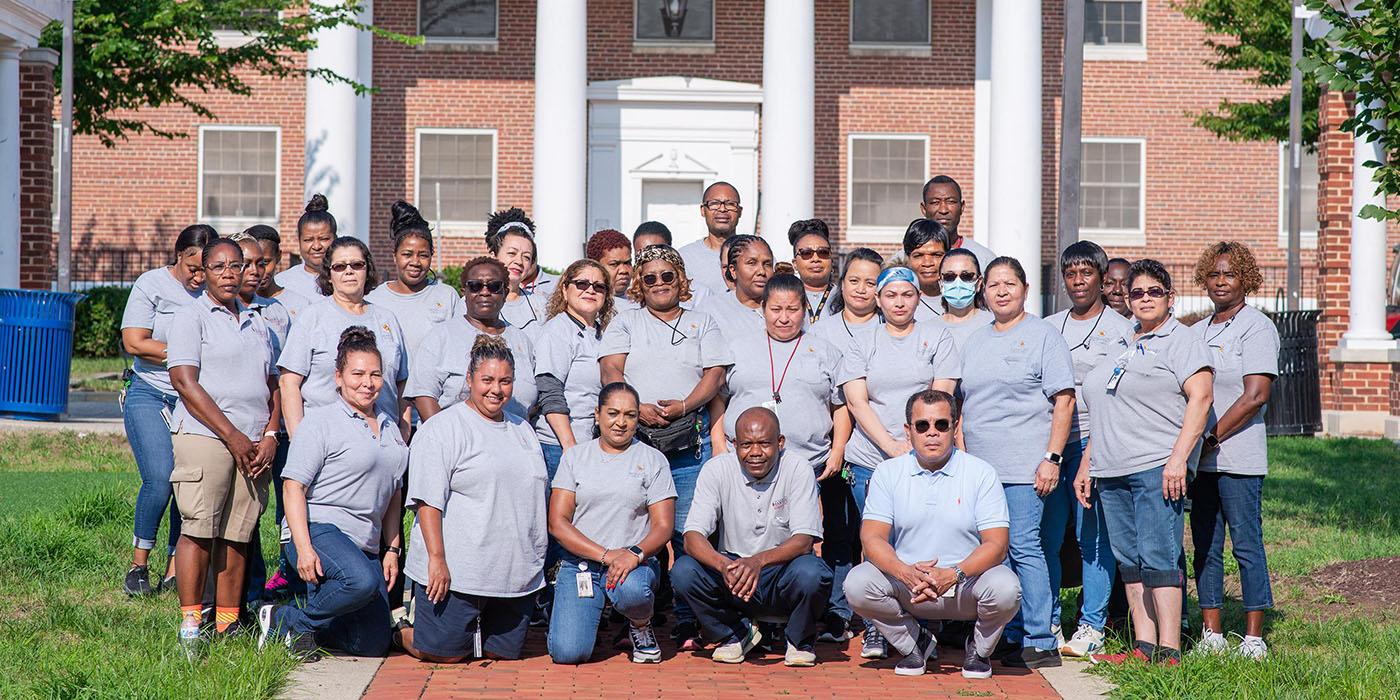 A large group of housekeeping staff in gray shirts posing in front of Baltimore Hall.