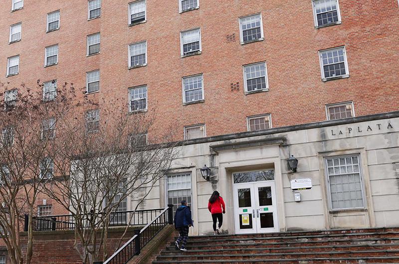 Exterior of brick La Plata Hall with white door frame and people walking up the steps.
