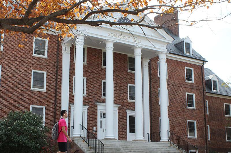 Exterior of  Somerset Hall, a brick residence hall with tall white columns and a student walking by.
