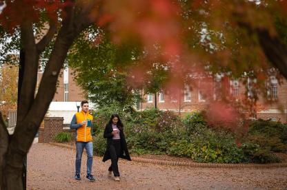 two students walking on campus on a fall day holding to-go coffee cups