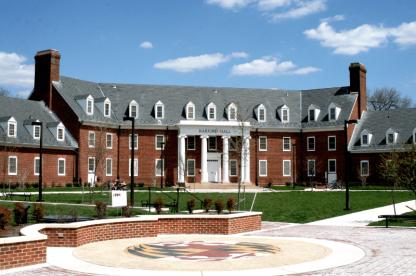 Exterior of Harford Hall, a brick building with white pillars and dormers behind a brick courtyard.
