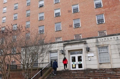 Exterior of brick La Plata Hall with white door frame and people walking up the steps.