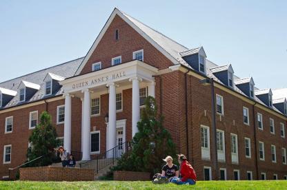 Exterior of Queen Anne's Hall, a brick residence hall with white columns and students sitting on the front lawn.
